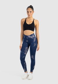 Sportivo nero con arricciatura sul davanti, abbinato a leggings blu navy con un leggero motivo astratto. Texture liscia, design aderente.