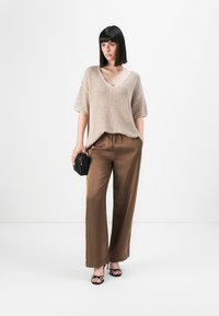 Beige strikket oversized genser, brune sateng brede bukser, svart håndveske, og svarte sandaler med remmer. Jevn tekstur, løs passform, og V-hals design.