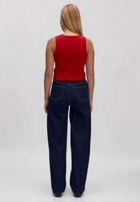 Rotes, geripptes Tanktop kombiniert mit hochtaillierten, locker sitzenden dunkelblauen Jeans. Verfügt über standardmäßige Gesäßtaschen und gerade Beine.