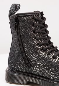 Stivale alla caviglia nero con superficie texture, chiusura con zip, design lace-up e suola chunky con scanalature visibili.