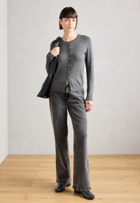 Gray button-up cardigan with a round neckline, paired with gray flared jeans. Model holds a black bag and wears dark shoes.