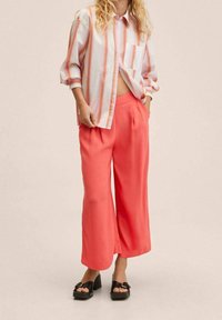 Katoenen shirt in een blend met roze en oranje strepen, gecombineerd met koraalrode wijde trousers. Zwarte plateau sandalen met gespdetails.