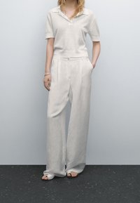 Vaaleanharmaa pellavapaita, jossa on lyhyet hihat, yhdistettynä leveisiin valkoisiin pellavahousuihin. Omistaa nappikiinnityksen ja taskut.