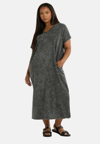 Harmaa, lyhythihainen maksimekko V-päällä, pehmeä rakenne, sivutaskut ja rento istuvuus, yhdistettynä mustiin sandaaleihin.