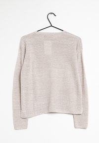 Vaalea beige neulottu pitkähihainen villapaita roikkuu mustassa hangessa valkoista taustaa vasten, nähtynä takaa.