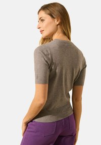 Pull gris à manches courtes en tissu lisse, avec un col rond et une coupe ajustée, associé à un pantalon violet.
