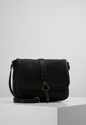Zwarte leren crossbodytas met frontklep, verstelbare schouderriem en goudkleurige gesp, liggend op een wit oppervlak.