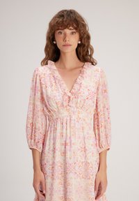 Robe à motifs floraux mettant en avant un décolleté en V, un col froncé, une taille élastique et de longues manches bouffantes dans des tons doux de rose et d'orange.