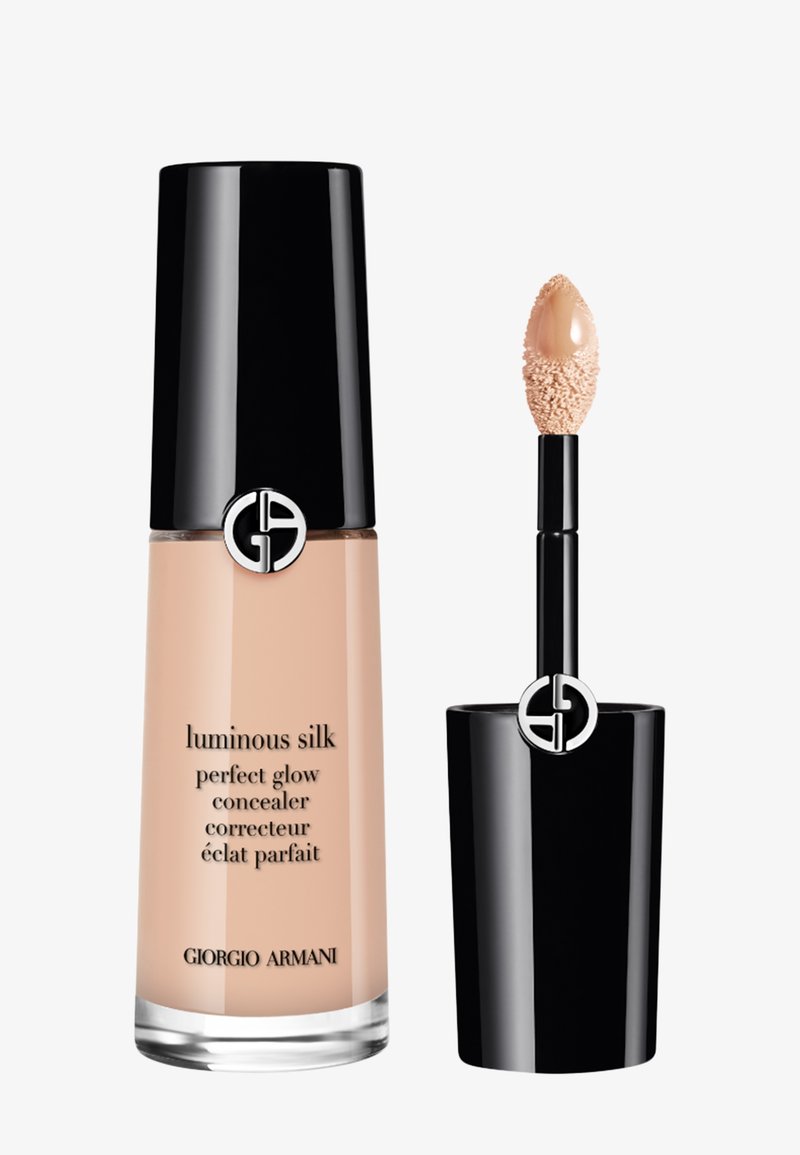 Flasche mit hellbeigem flüssigem Concealer mit schwarzem glänzendem Deckel und Applikatorstab mit einem schmetterlingsförmigen Applikator, der mit Produkt bedeckt ist.