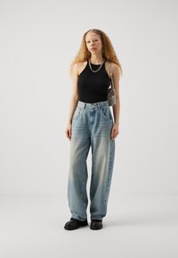 Black ribbed halter top paired with light blue oversized jeans. Accessories include a metallic chain necklace and a textured black bag.