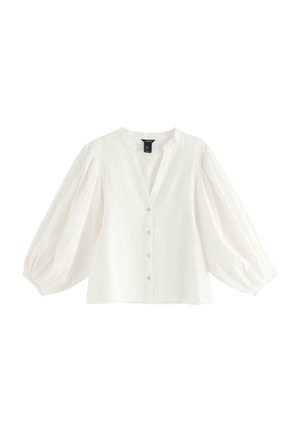 Vit blus med v-hals, knappframsida och voluminösa långa ärmar. Den texturerade tyget erbjuder ett subtilt mönster genom hela plagget.