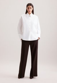 Camicia bianca con colletto, con bottoni sul davanti, abbinata a pantaloni larghi marroni scuri. Tessuto liscio e vestibilità sartoriale.