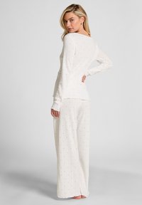 Witte loungewear set met lange mouwen en wijde pijpen, gemaakt van textuurstof gemarkeerd met kleine blauwe accenten.