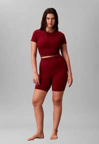 Rød strikket activewear sæt bestående af kortærmet top og cykelshorts. Geometrisk mønster, elastisk linning med Calvin Klein branding.