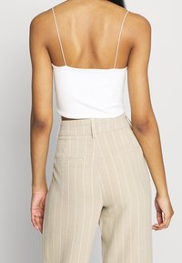 Top corto bianco a coste con spalline sottili abbinato a pantaloni a righe beige a vita alta con chiusura con zip e tasche posteriori.