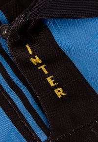 Blauwe stof met zwarte accenten en horizontale strepen. Zwart etiket toont het woord "INTER" in vette gele letters.