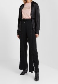 Musta satiinipaita, pinkki graafinen t-paita ja mustat leveälahkeiset housut, joissa on painonapit ja sivulla logo. Yhdistetty mustiin korkokenkiin.