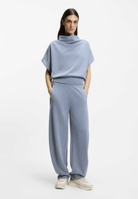 Light blue loungewear set featuring a loose-fitting, cowl-neck top and wide-leg pants, made of a smooth fabric with subtle stitching details.