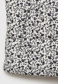 Čierny kvetinový vzor na bielom textile, so silnou textúrou a vyšívanými detailmi. Obsahuje viditeľnú vrecko na jednej strane.