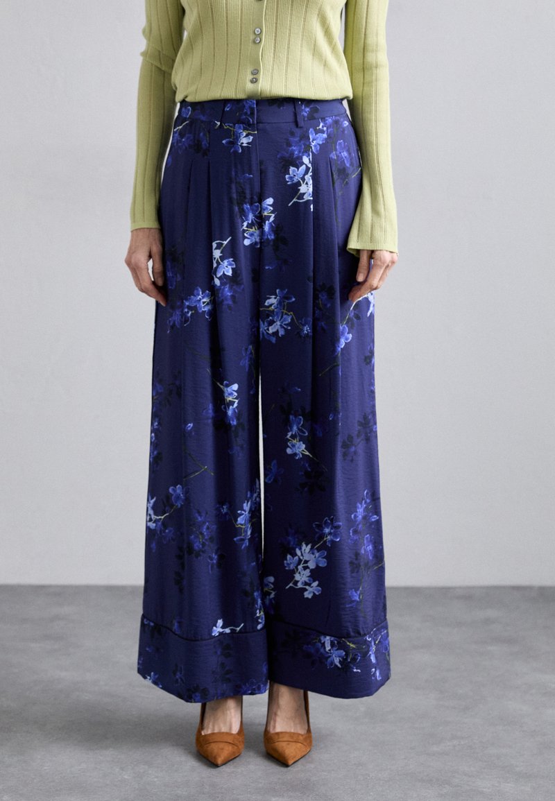 Navy floral wide-leg trousers with purple and blue patterns, featuring a smooth texture and a tailored fit, paired with brown pointed heels.