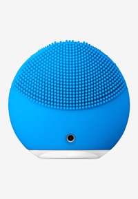 Silicone ansiktsrensingsenhet i lys blå. Rund form med teksturerte prikker for eksfoliering, med en liten åpning nederst.