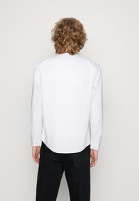 Witte langarmshirt met een puntkraag, knopen en een afgeronde zoom. De stof lijkt glad en licht van gewicht.