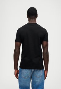 Μαύρη κοντομάνικη μπλούζα από βαμβάκι, με στρογγυλή λαιμόκοψη και χαλαρή εφαρμογή, φορεμένη με ανοιχτό μπλε τζιν παντελόνι.