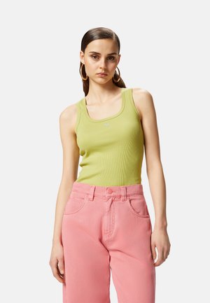 Top verde a costine con scollatura rotonda, abbinato a jeans rosa a vita alta con tasche frontali e chiusura a bottone.