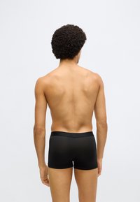 Fekete boxeralsó sima, rugalmas anyagból; a derékpánt egyszínű és szorosan illeszkedik. A nézet hátulról van.
