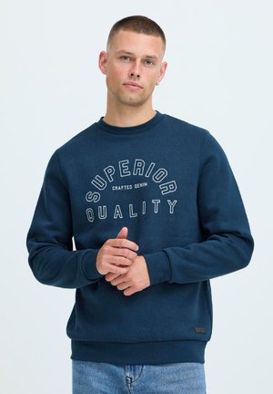 Mørkeblå hettegenser laget av bomullsblanding, med ribbestrikkede ermer og kant. Frontdesignet inkluderer teksten "SUPERIOR QUALITY" i hvitt.