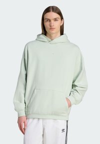 Svetlozelená mikina s kapucňou, predn�ým vreckom, rebrovanými manžetami a vyšitým logom na hrudi. Skombinovaná s bielymi nohavicami s čiernymi pruhmi.