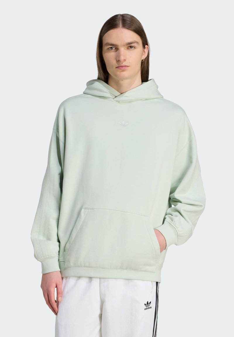 Svetlozelená mikina s kapucňou, predným vreckom, rebrovanými manžetami a vyšitým logom na hrudi. Skombinovaná s bielymi nohavicami s čiernymi pruhmi.