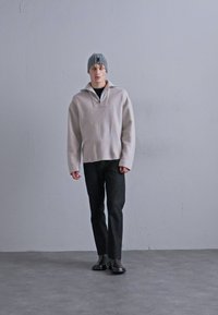 Light gray, soft material pullover with a half-zip collar, worn over a black t-shirt and paired with dark jeans and boots. Gray knitted beanie.
