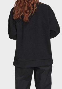 Svart fleece oversize sweatshirt med en texturerad yta och ribbad fåll, i kombination med matchande svarta byxor, sedd bakifrån.