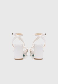 Sandali bianchi con tacco quadrato, strap per incroci e decorazioni floreali sul retro. Superficie liscia e chiusura con fibbia alla caviglia.