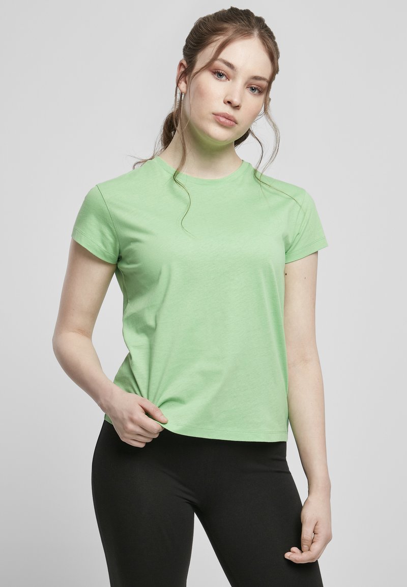 Lys grøn bomulds T-shirt med korte ærmer, rund halsudskæring og afslappet pasform, kombineret med sorte leggings. Glat tekstur, minimalistisk design.