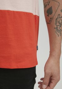 Raudona ir šviesiai rožinė dryžuota marškinėliai iš minkštos medvilnės. Tiesus apatinis kraštas su maža labelė šone. Audinys su tekstūra ir patogus prigludimas.
