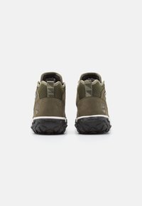 Chaussures de randonnée en daim vert et mesh avec une semelle en caoutchouc noir texturé, présentant un logo et une languette à motif au niveau du talon.