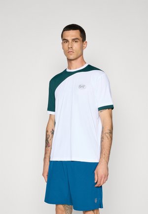 White and green short-sleeve sports shirt with a rounded neckline and EA7 logo, worn with blue shorts. Smooth texture and athletic fit.