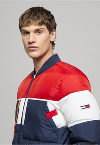 Prešívaná bombardérska bunda v červenej, bielej a námorníckej farbe so zipsom vpredu, rebrovaným golierom a nášivkou s logom na hrudi. Má cvočkové vrecko a textúrovanú tkaninu.