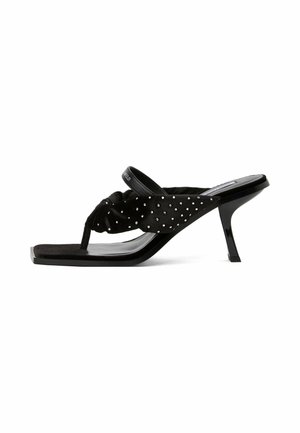 Sandale noire à talon haut avec bout carré, sangle nouée décorée de petits clous et talon étroit de hauteur moyenne.