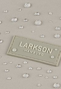 Szürke textúrájú szövet, amelyen világos, gyémántszerű díszítések találhatók, valamint egy téglalap alakú címke, amelyen fehér betűkkel az "LARKSON HAMBURG" felirat olvasható.