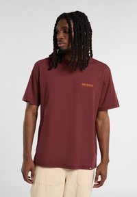 Bordové tričko s krátkým rukávem a klasickým výstřihem, na levé části hrudi má malé oranžové logo. Vyrobeno z hladkého materiálu a volného střihu.