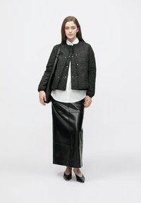 Fekete steppelt dzseki patentos gombokkal, alatta fehér galléros ing, hozzá hosszú fekete bőr szoknya és fekete cipő.