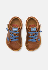 Chaussures en cuir marron avec des lacets bleus, bout rond, détails en couture et une étiquette de logo sur la languette. Semelle en caoutchouc.