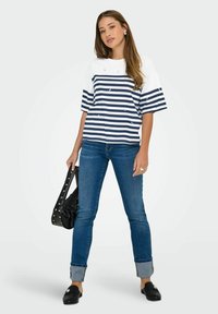 Haut à manches courtes rayé en blanc et marine, associé à un jean bleu retroussé et des mocassins noirs, avec un sac à bandoulière noir.