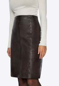 Brązowa skórzana spódnica ołówkowa o gładkiej fakturze, z dopasowanym krojem i szwem z przodu. Połączona z jasnym topem.