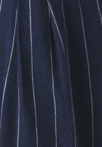 Niebieski materiał z pionowymi białymi paskami, o teksturowanym, tkanym wyglądzie. Tkanina miękko opada, podkreślając ruch i przepływ.