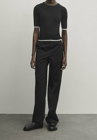 Top nero a maniche corte a coste con finitura testurizzata, abbinato a pantaloni neri larghi e scarpe in pelle scura.