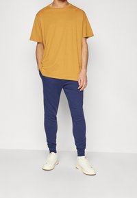 Hořčicové tričko s krátkým rukávem v kombinaci s námořnickými joggingovými kalhotami. Kalhoty mají slim-fit střih, elastické manžety a outfit doplňují bílé tenisky.